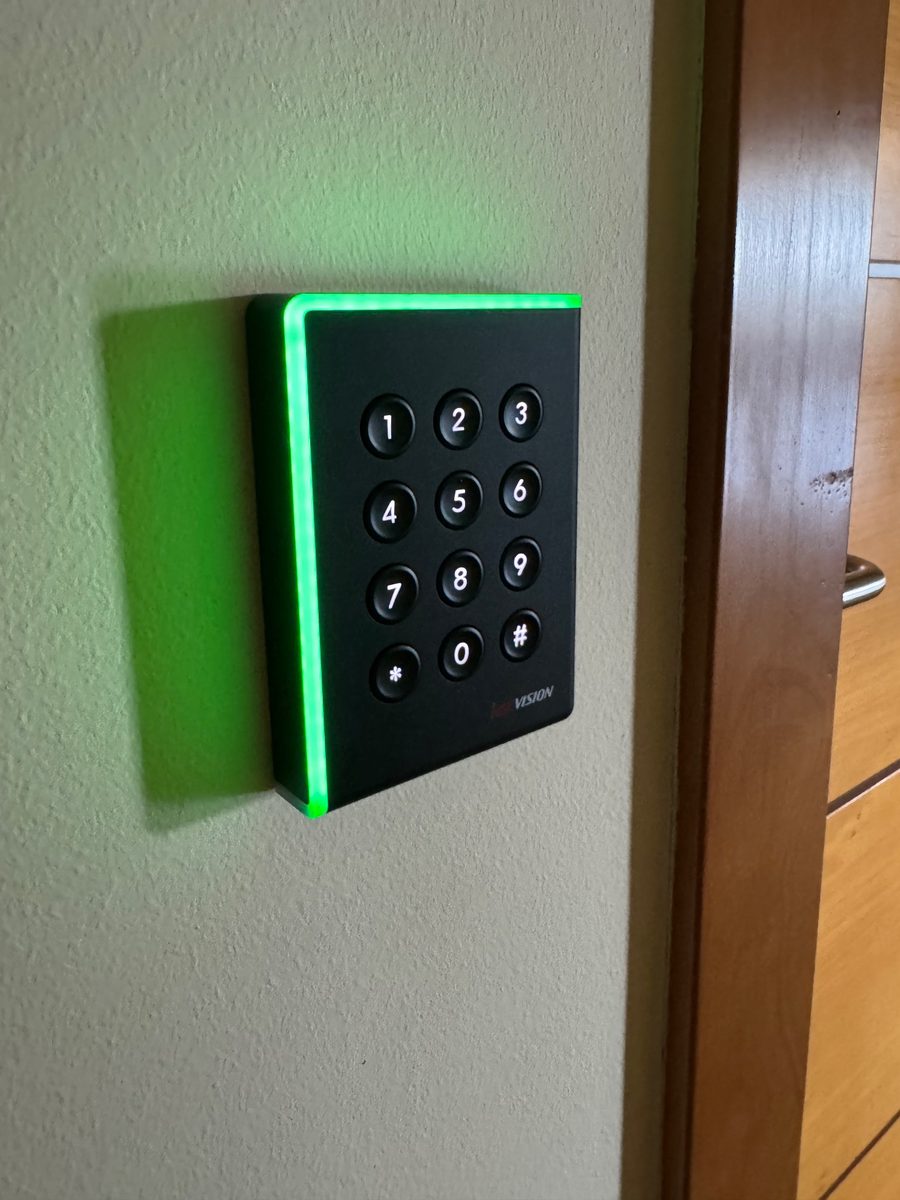 Lector de tarjetas con teclado iluminado en verde junto a una puerta de las oficinas